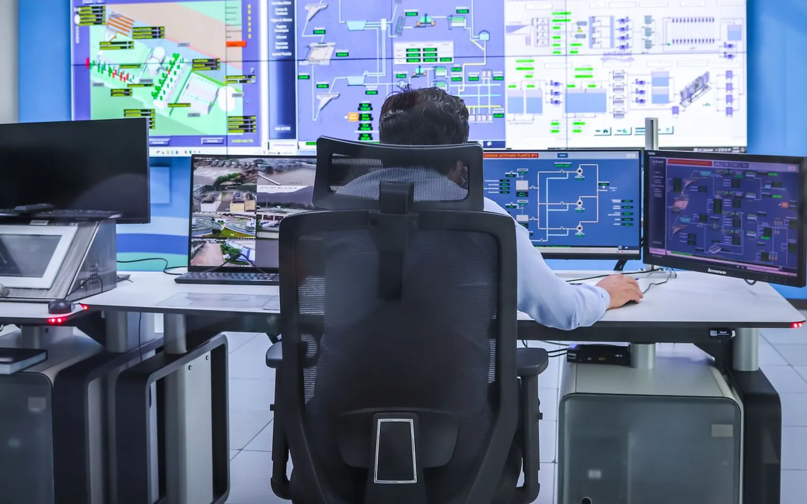 An operator at a desk of monitors, facing a large wall of displays