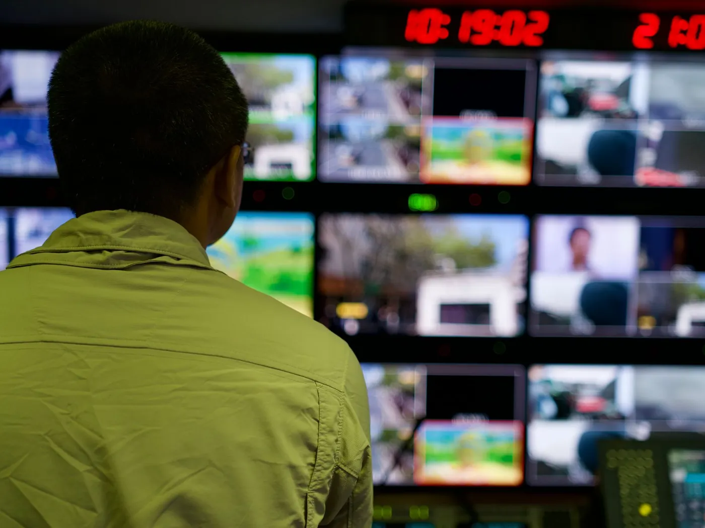 A person seen from behind, facing a wall of video monitors