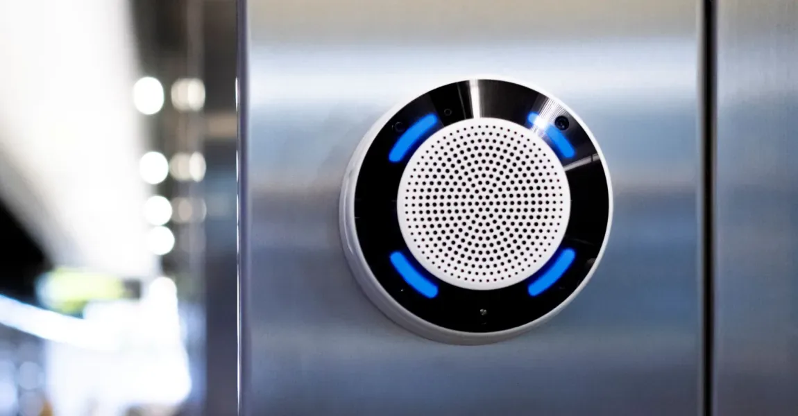 A white Axis speaker mounted on a wall, with a blue light on the front.